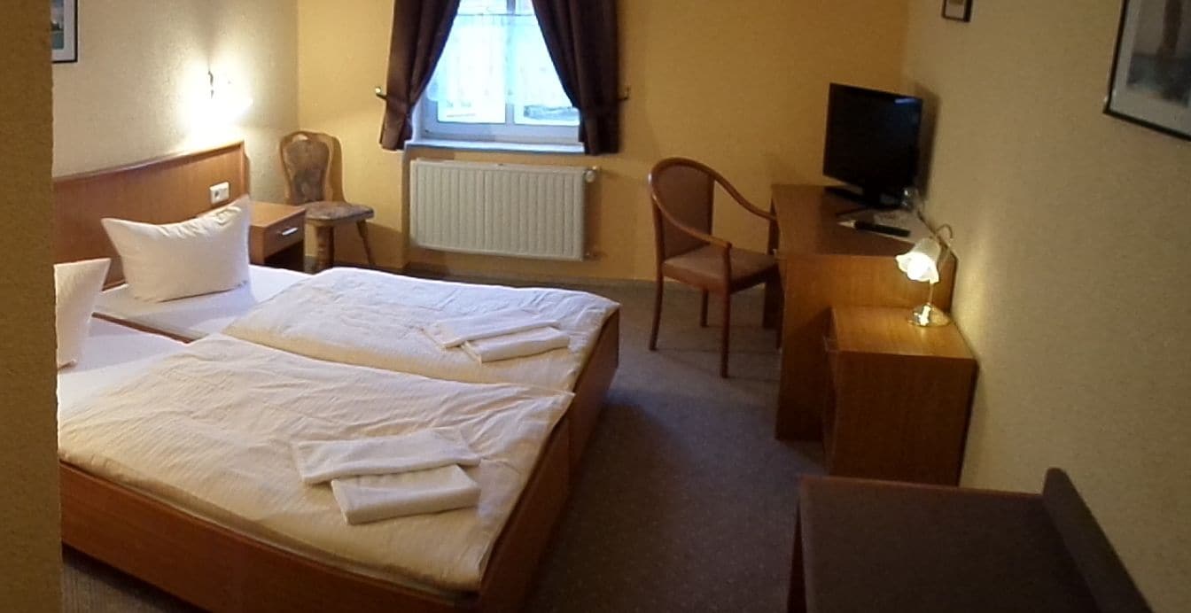 Une chambre d’hôtel avec deux lits, un bureau, une chaise, une télévision et une fenêtre avec des rideaux.