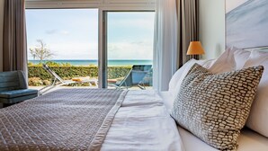 A hotel room with a large bed, a view of the ocean, and a balcony with chairs. - Hotel Strandidyll (Groemitz)
