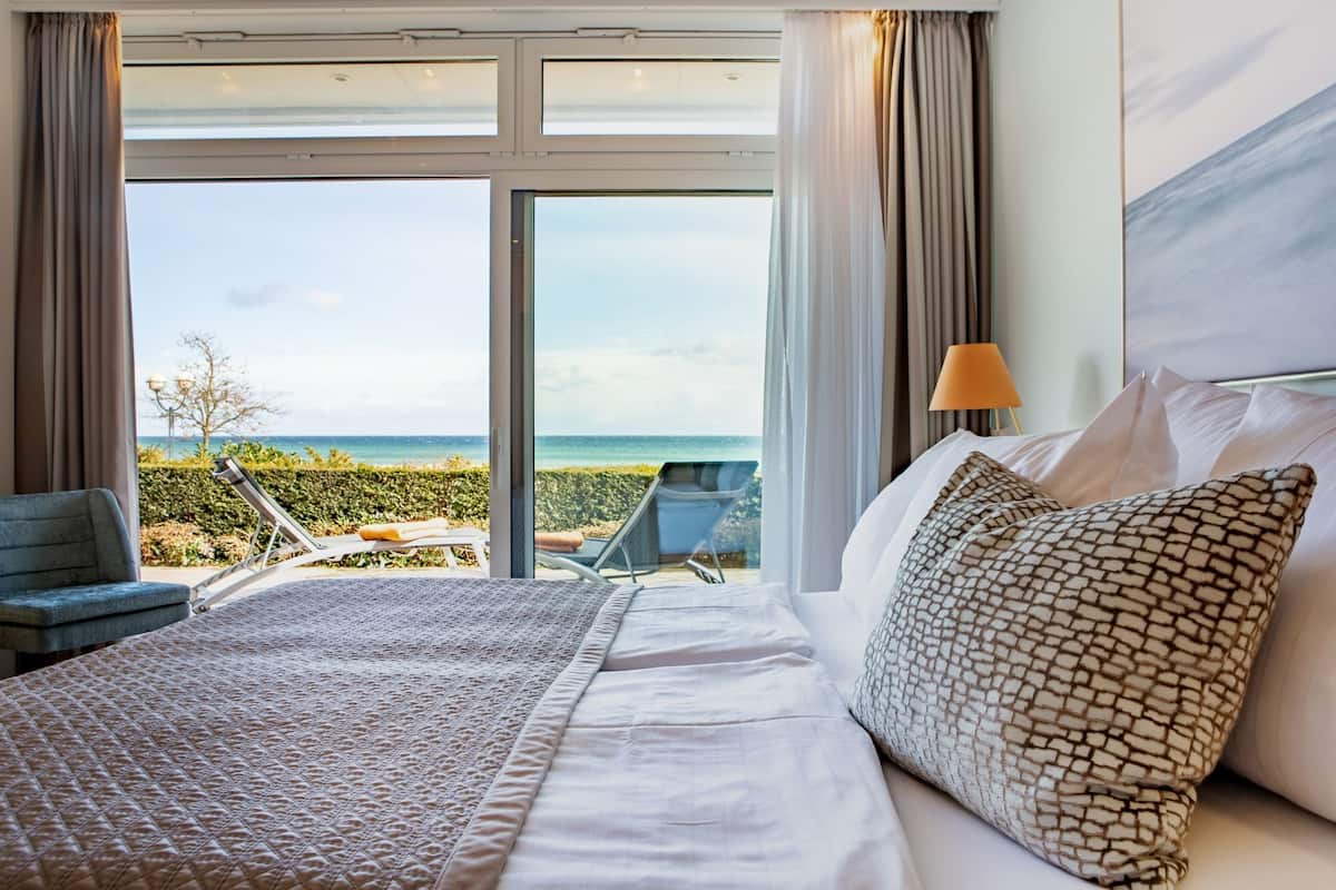A hotel room with a large bed, a view of the ocean, and a balcony with chairs.