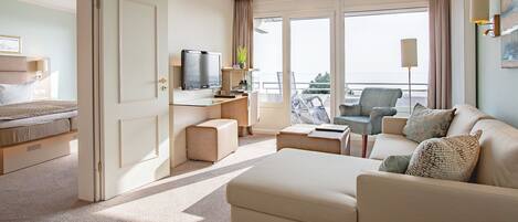Een hotelkamer met een bed, een bank, een televisie, een balkon met een stoel en een bureau met een lamp.