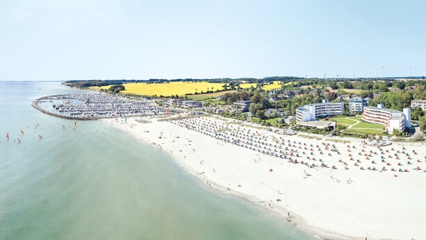 A coastal town with a beach, marina, and residential buildings. - Hotel Strandidyll (Groemitz)