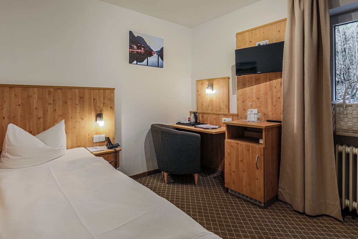 A hotel room with a bed, a desk, a chair, a mirror, and a window with curtains.