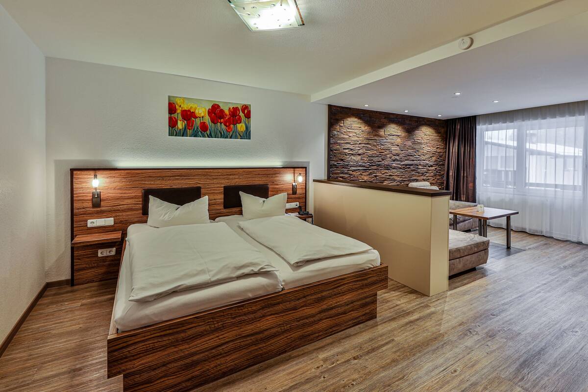 A modern bedroom with a wooden bed, a nightstand, a painting of tulips, a stone accent wall, and a window with curtains.