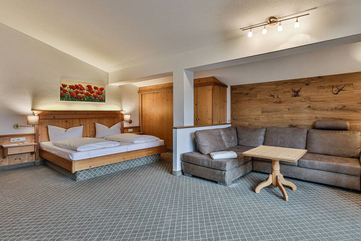 A bedroom with a bed, a sofa, a small table, a lamp, and a wooden wall with a picture.