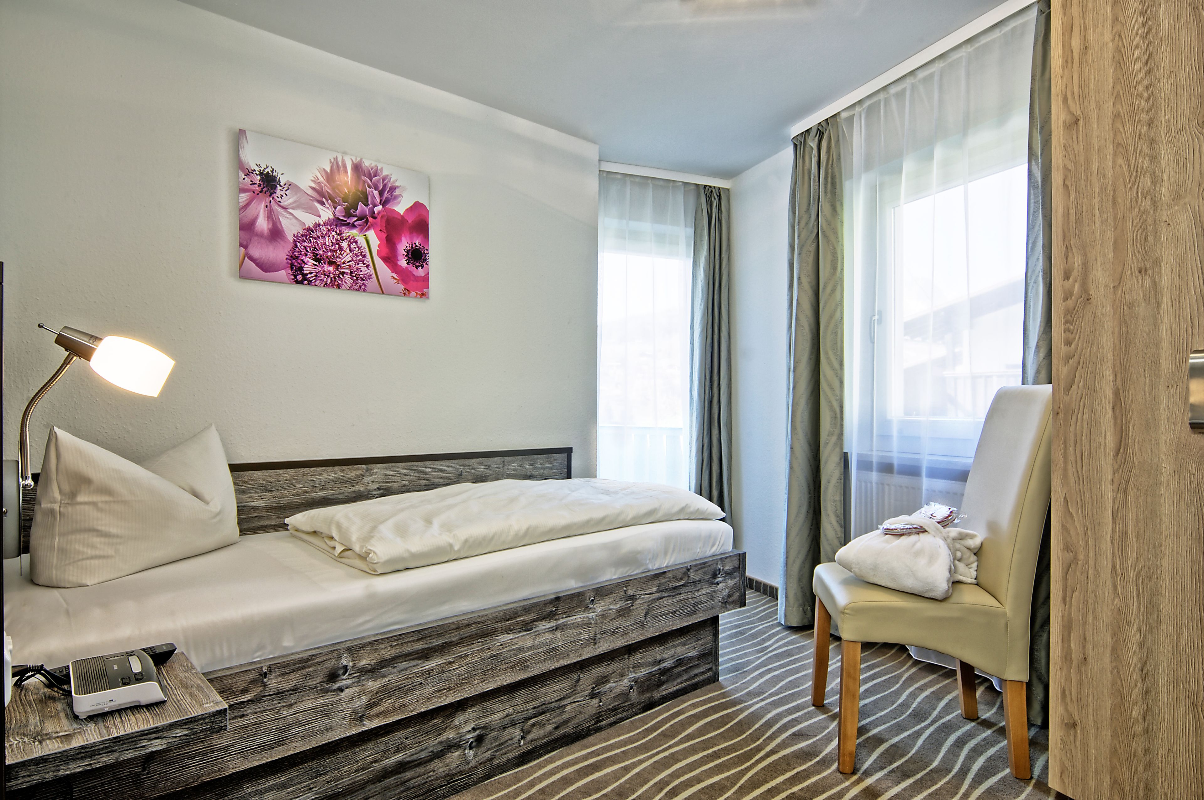 A modern hotel room with a bed, a chair, a lamp, and a window with curtains.