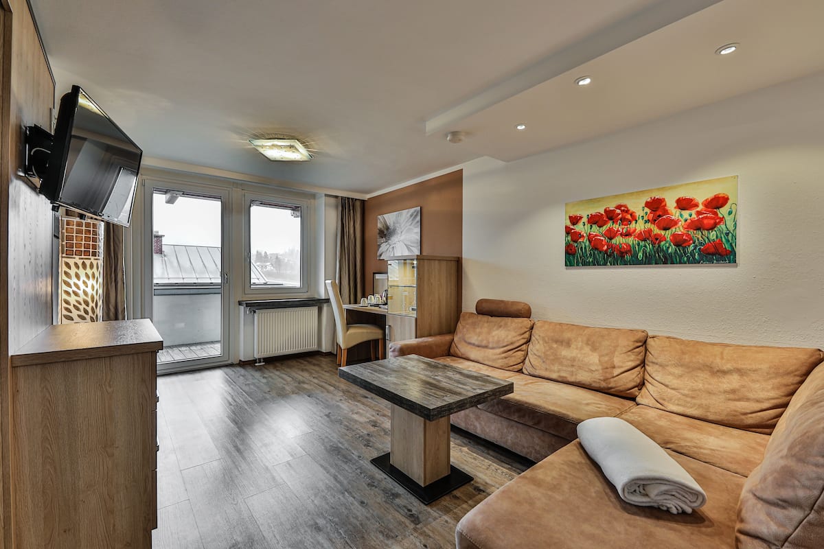 A modern living room with a sofa, a wooden table, and a painting of red flowers on the wall.