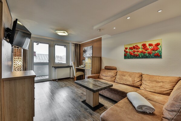 A modern living room with a sofa, a wooden table, and a painting of red flowers on the wall. - Alpenhotel Fischer - Adults Only (Berchtesgaden)