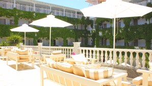 A sunlit outdoor seating area with white furniture and umbrellas, surrounded by a white balustrade and greenery. - Olympic Kosma Hotel (Kassandra)