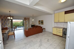 A modern kitchen with yellow cabinets, a dining area with a table and chairs, and a living room with a sofa. - Olympic Kosma Hotel (Kassandra)