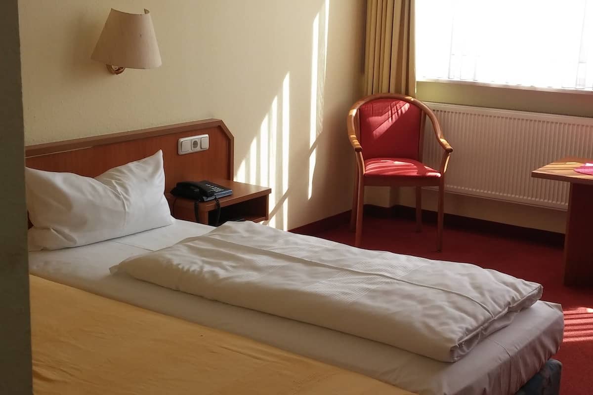 A hotel room with a bed, a desk, a chair, a lamp, and a window with curtains.