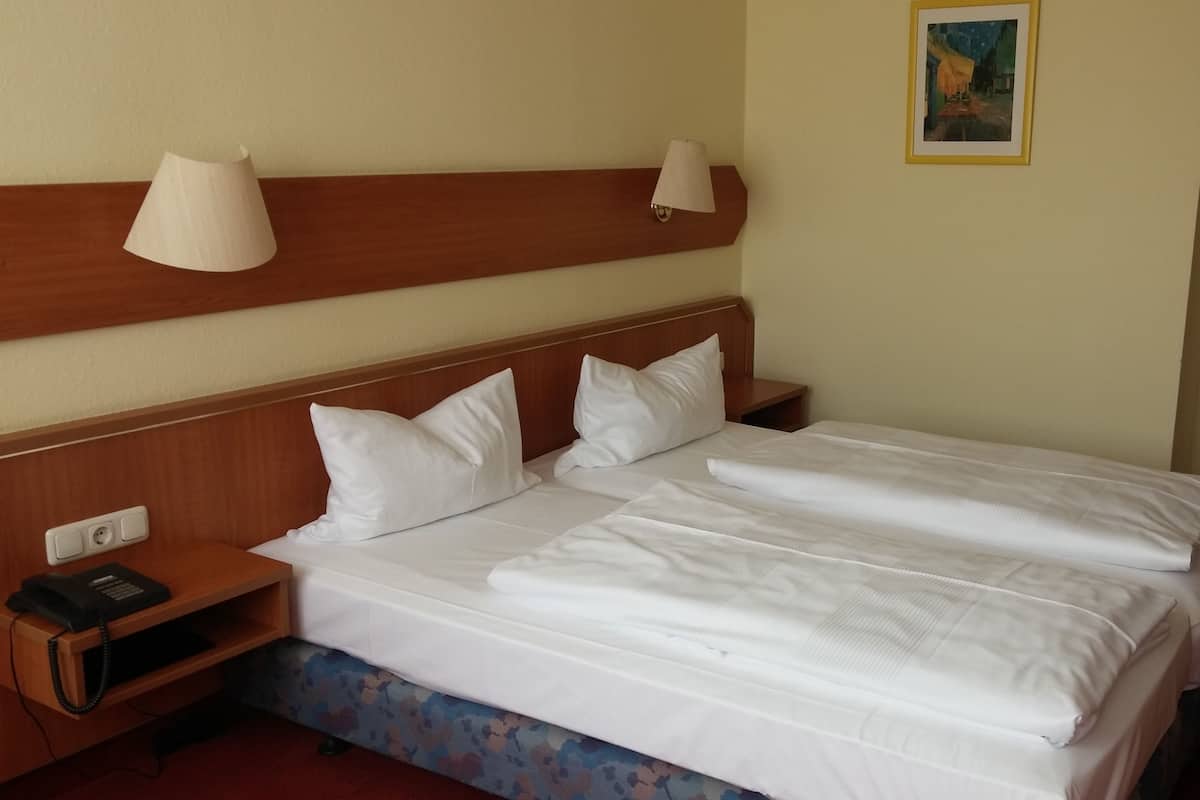 A hotel room with a wooden headboard, two bedside lamps, a telephone, and a framed picture on the wall.
