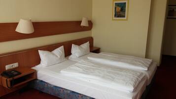 A hotel room with a wooden headboard, two bedside lamps, a telephone, and a framed picture on the wall.