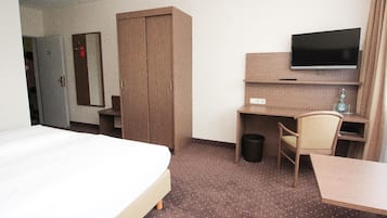 A hotel room with a bed, a desk, a chair, a television, and a wardrobe.