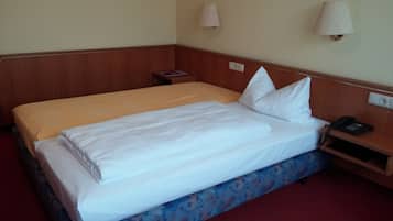 A hotel room with a double bed, a bedside table with a lamp, a phone, and a wall socket.