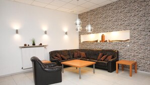 A modern living room with a black leather sofa, two wooden coffee tables, and a stone wall with a framed picture. - Hotel Berliner Ring (Bamberg)