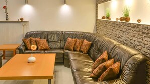 A modern living room with a leather sectional sofa, two pendant lights, a wooden coffee table, and a brick accent wall. - Hotel Berliner Ring (Bamberg)