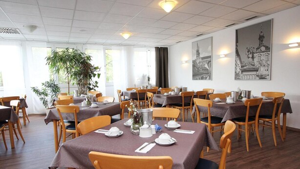 A dining area with multiple tables set for service, wooden chairs, and large windows allowing natural light. - Hotel Berliner Ring (Bamberg)
