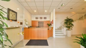 A reception area with a wooden counter, a black mat, a staircase, and potted plants. - Hotel Berliner Ring (Bamberg)