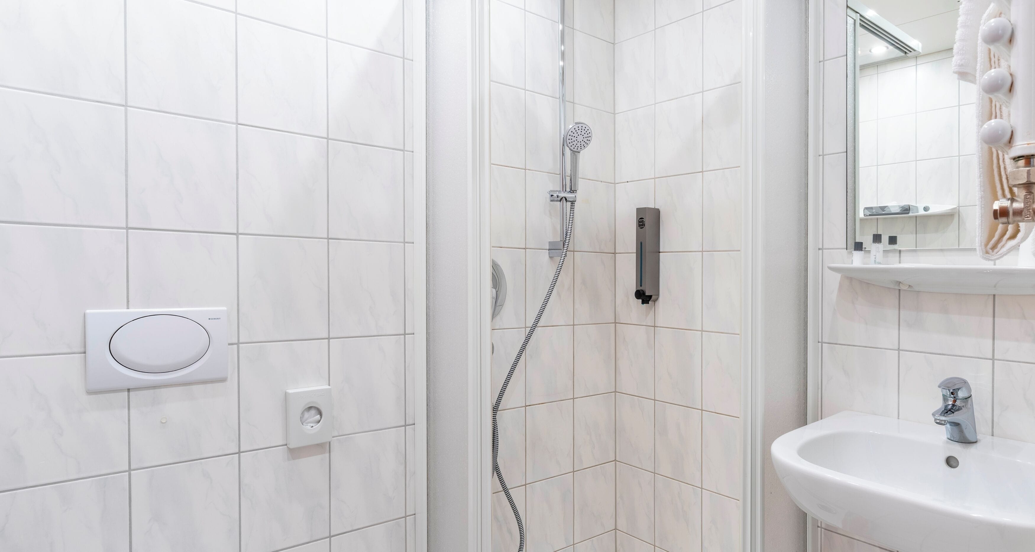 Een moderne badkamer met witte tegels, een douche met handdouche, een ingebouwd toilet en een wastafel met spiegel erboven.