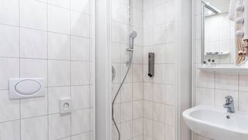 Een moderne badkamer met witte tegels, een douche met handdouche, een ingebouwd toilet en een wastafel met spiegel erboven.