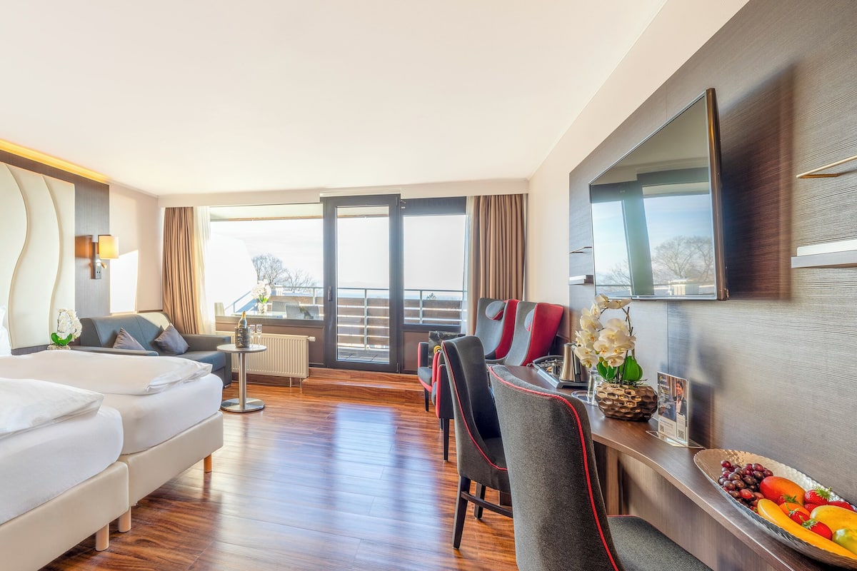 Une chambre d’hôtel avec un grand lit, un canapé, une table à manger avec des chaises, une télévision et un balcon avec vue.