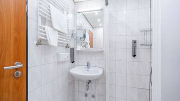 Ein Badezimmer mit Holztür, weißen Fliesenwänden, einem Waschbecken, einem Spiegel und einem Handtuchhalter.