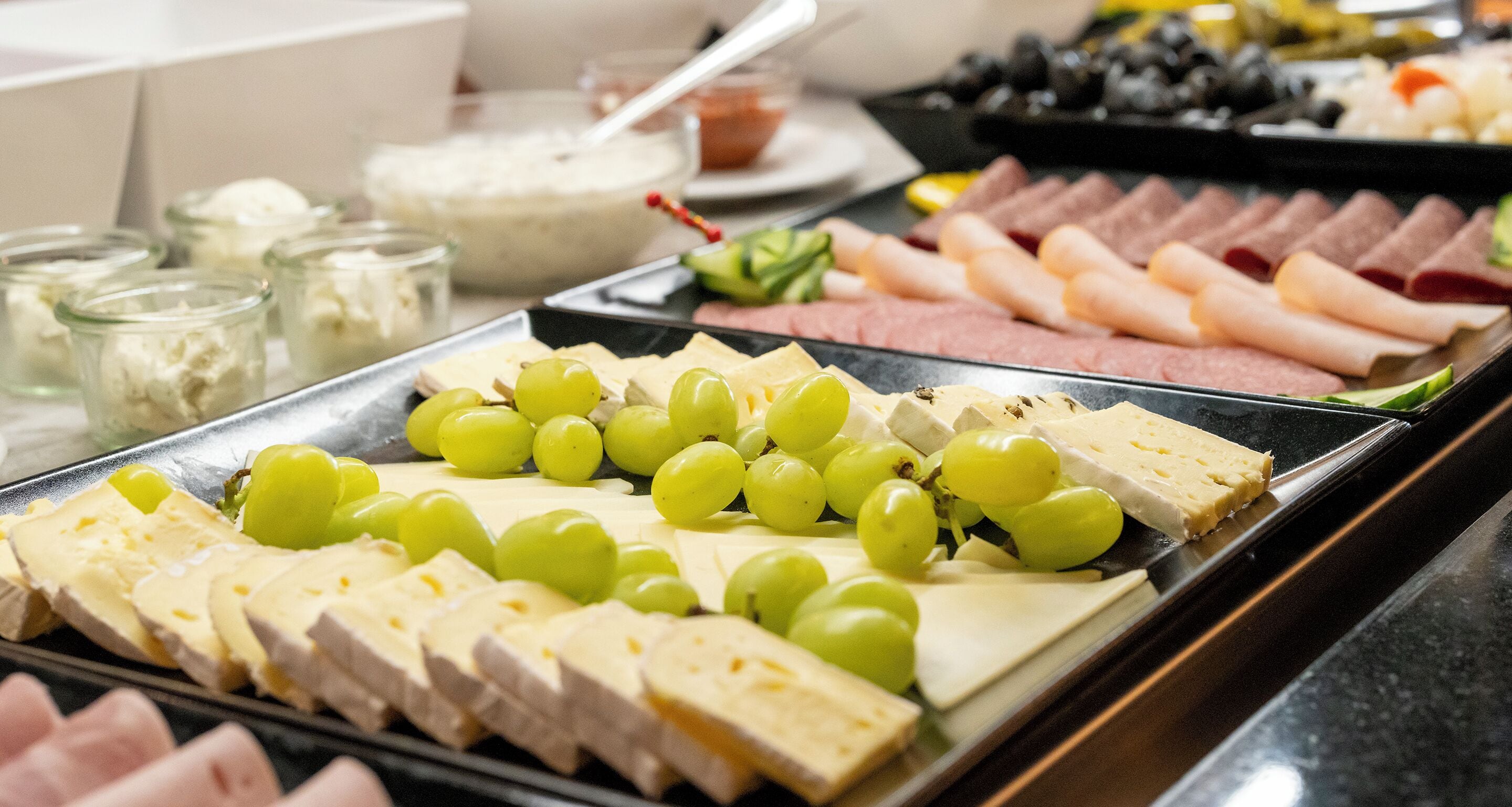 A buffet with various cheeses, grapes, and meats.