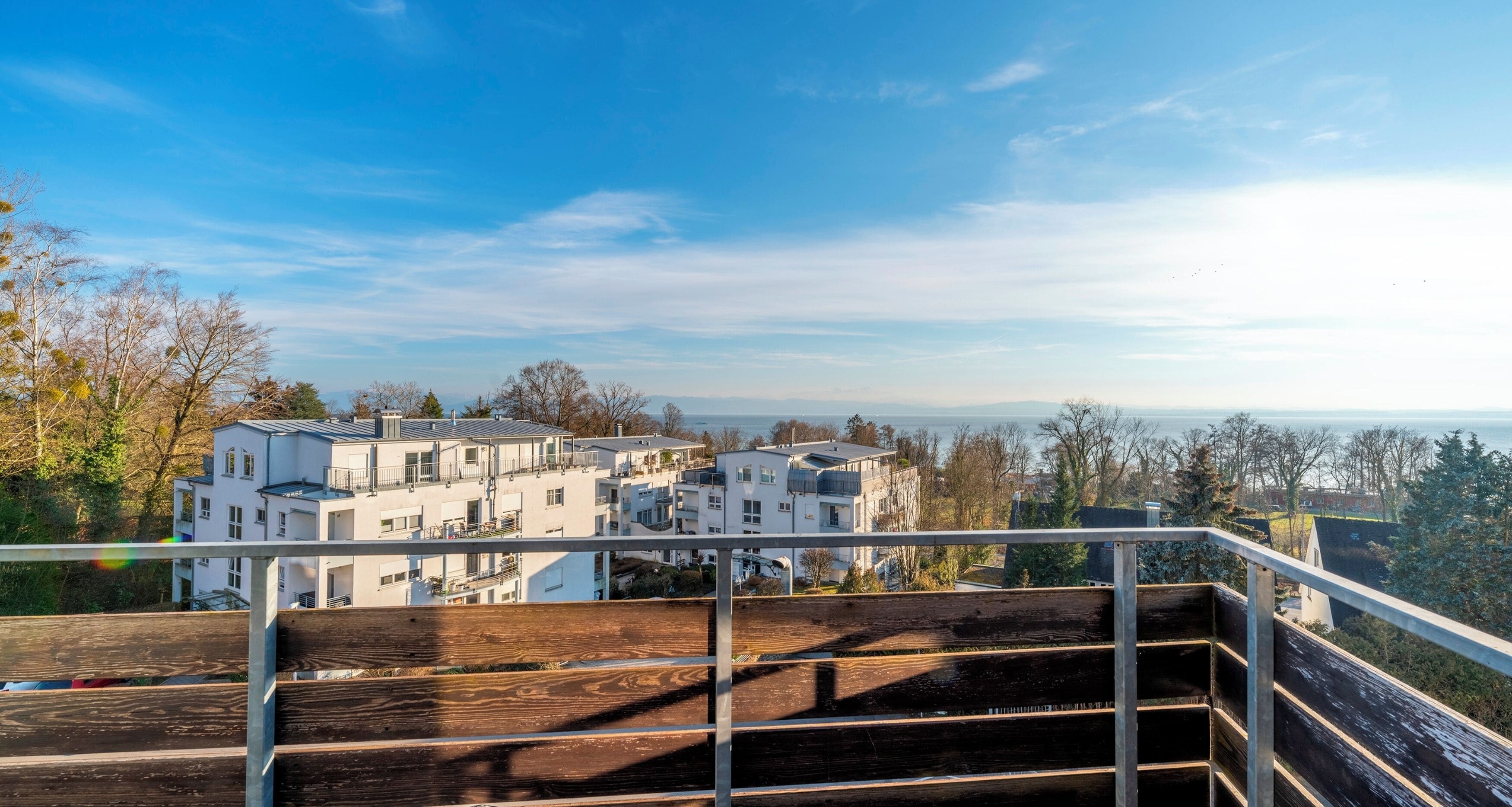Área residencial com edifícios brancos, um deck de madeira e vista clara para o mar.