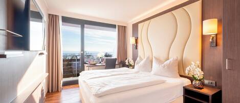 Ein Hotelzimmer mit einem großen Bett, einem Schreibtisch, einem Fernseher und Blick auf die Stadt.