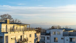 Ein mehrgeschossiges Wohngebäude mit Balkonen, großen Fenstern und Blick auf Berge im Hintergrund.