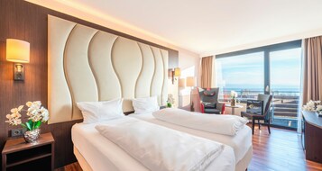 Quarto de hotel com uma cama grande, uma escrivaninha, uma cadeira e vista para a cidade.