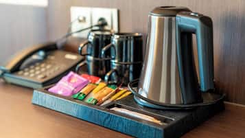 A coffee station with a coffee maker, a phone, and some snacks on a wooden surface.
