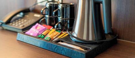 A coffee station with a coffee maker, a phone, and some snacks on a wooden surface.