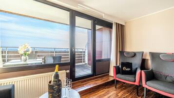 A balcony with a view, a table with a bottle and glasses, and two chairs with a bag on one.