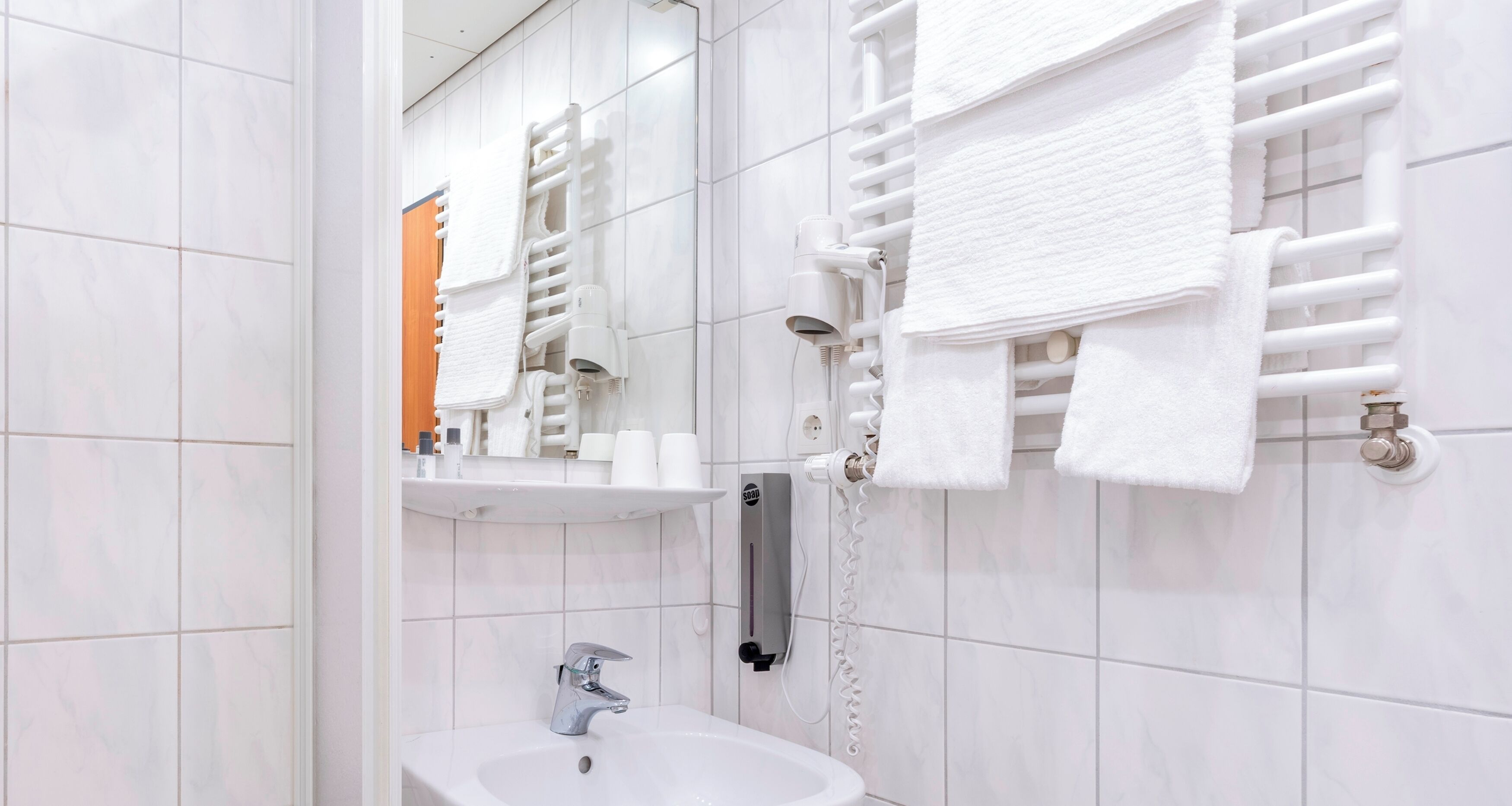 A bathroom with a white sink, a mirror, a towel rack, and a towel warmer.