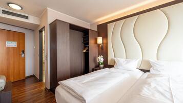 A hotel room with a large bed, a wardrobe, a bedside table with a lamp, and a wooden door.