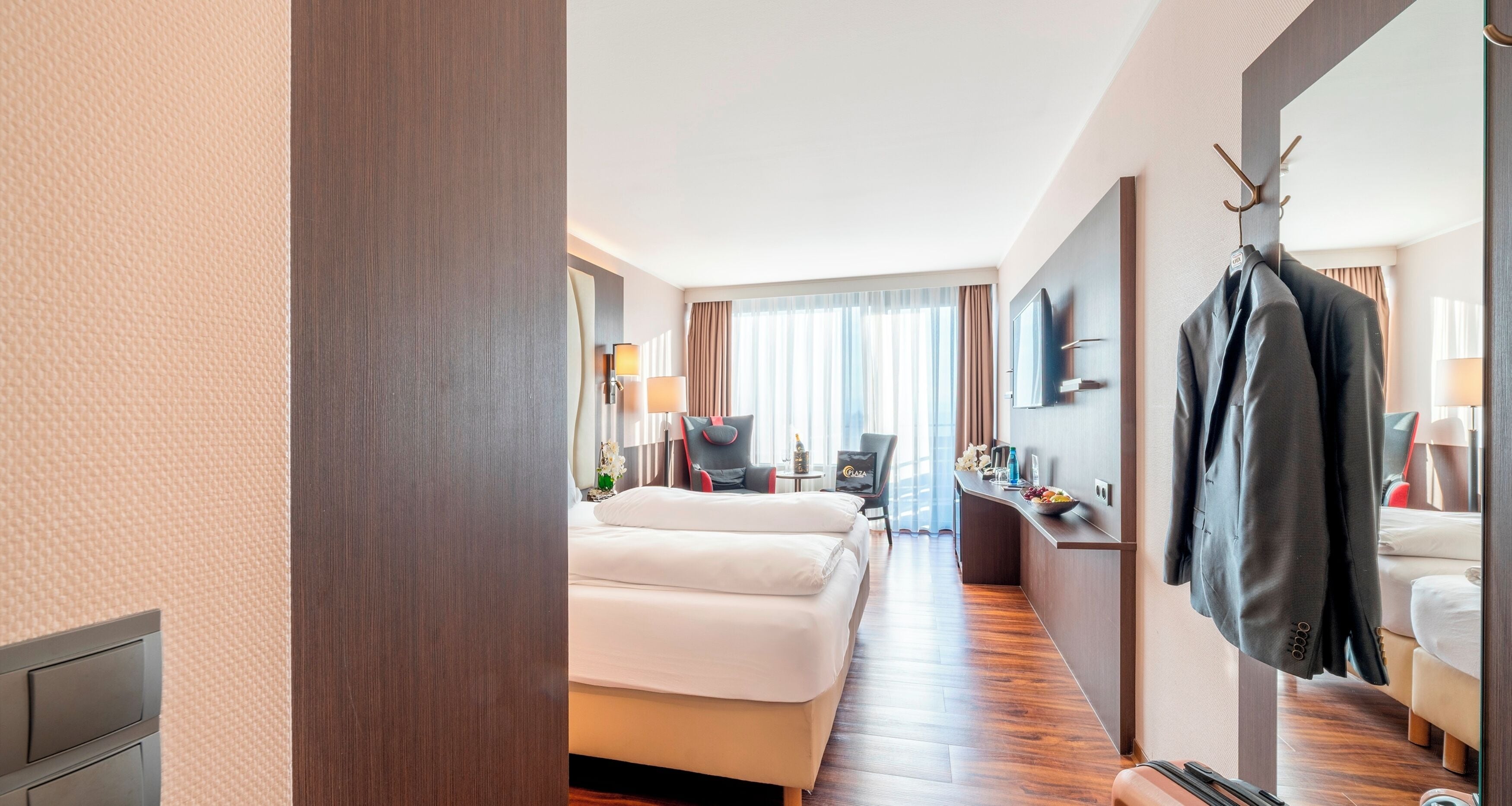 Habitación de hotel con cama, escritorio, silla, espejo y perchero.