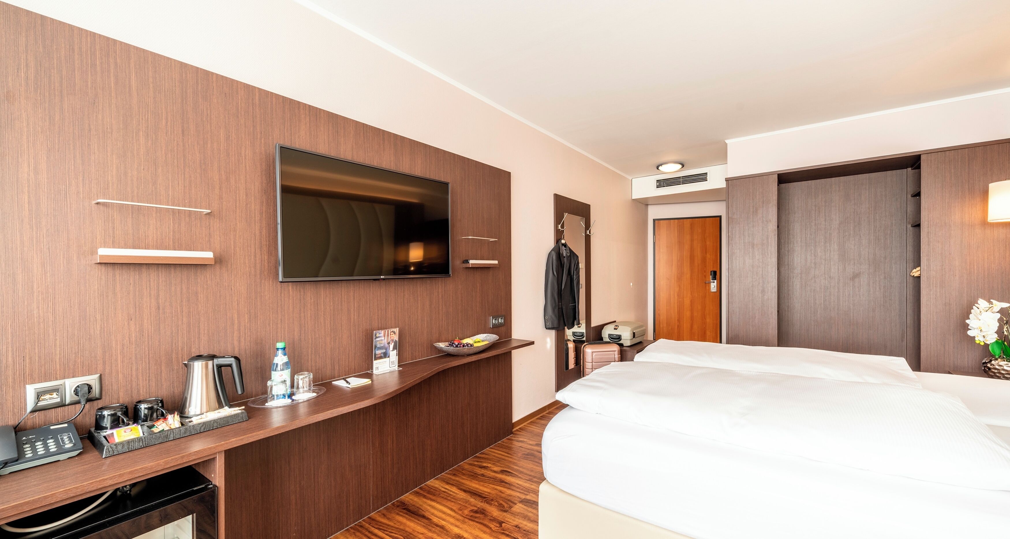 Habitación de hotel con escritorio de madera, televisor de pantalla plana, cama y armario.