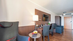 Ein Hotelzimmer mit einer Couch, Sesseln, einem kleinen Tisch mit Früchten, einer Lampe und einem Spiegel an der Wand.