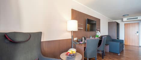 Habitación de hotel con sofá, sillas, una mesita con fruta, una lámpara y un espejo en la pared.