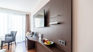 Ein modernes Hotelzimmer mit Schreibtisch aus Holz, einem Sessel, einem großen Spiegel und einer Obstschale.