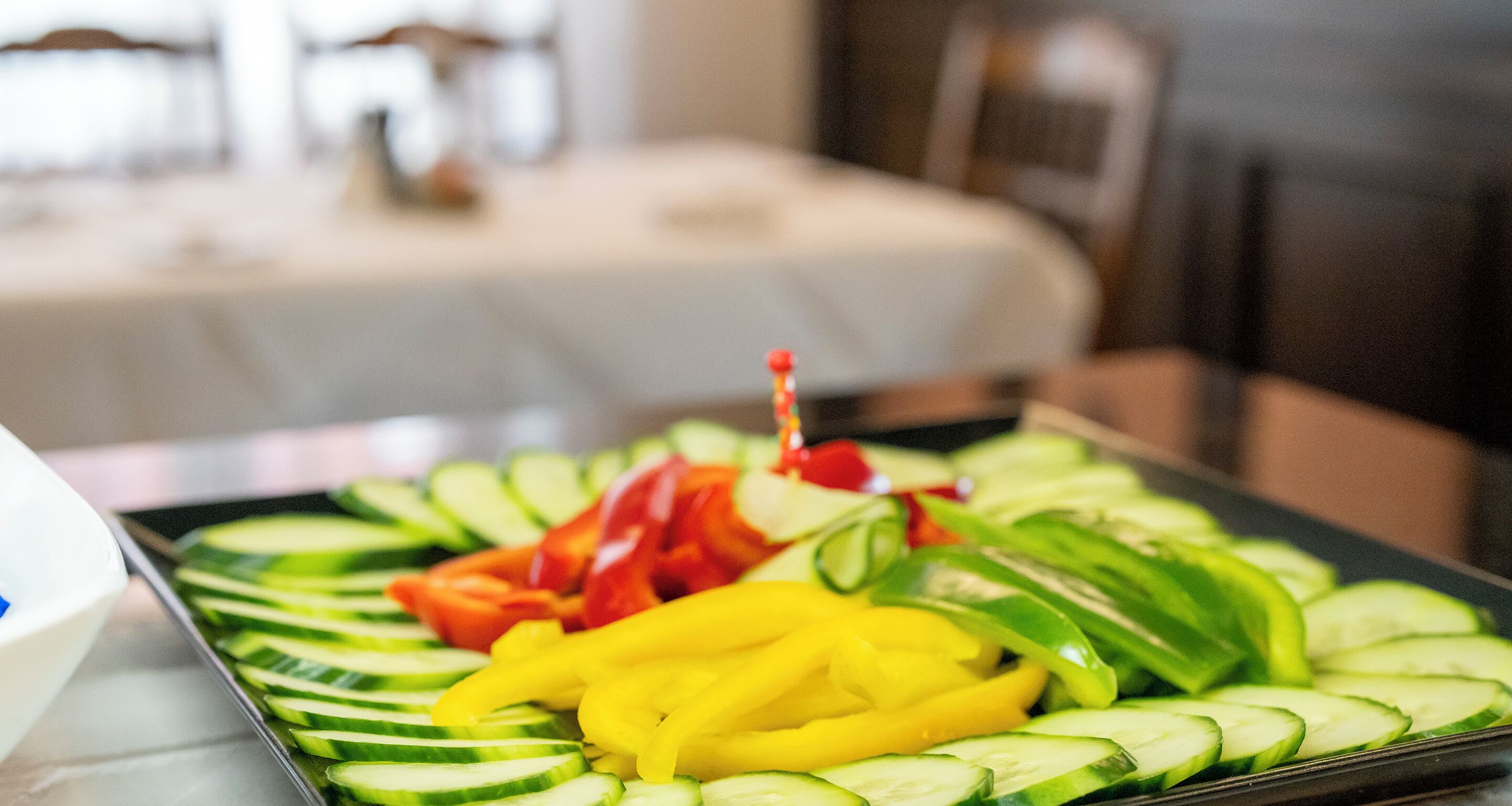 A tray of sliced vegetables including cucumbers, red bell peppers, and yellow bell peppers.