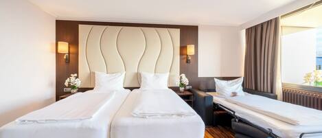 A hotel room with two beds, a sofa, a nightstand, and a window with curtains.