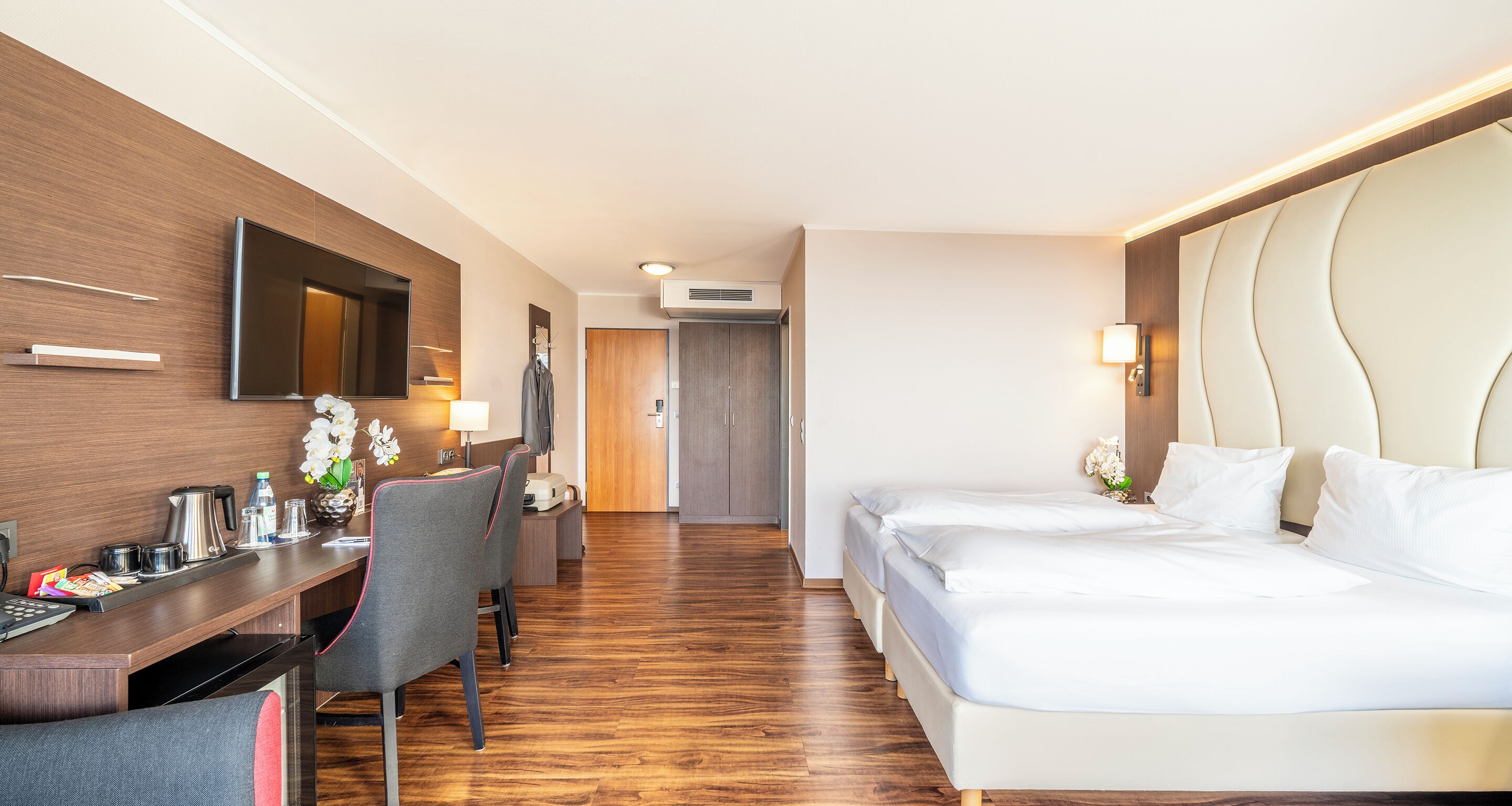 Una habitación de hotel con un escritorio de madera, una cama y un televisor montado en la pared.