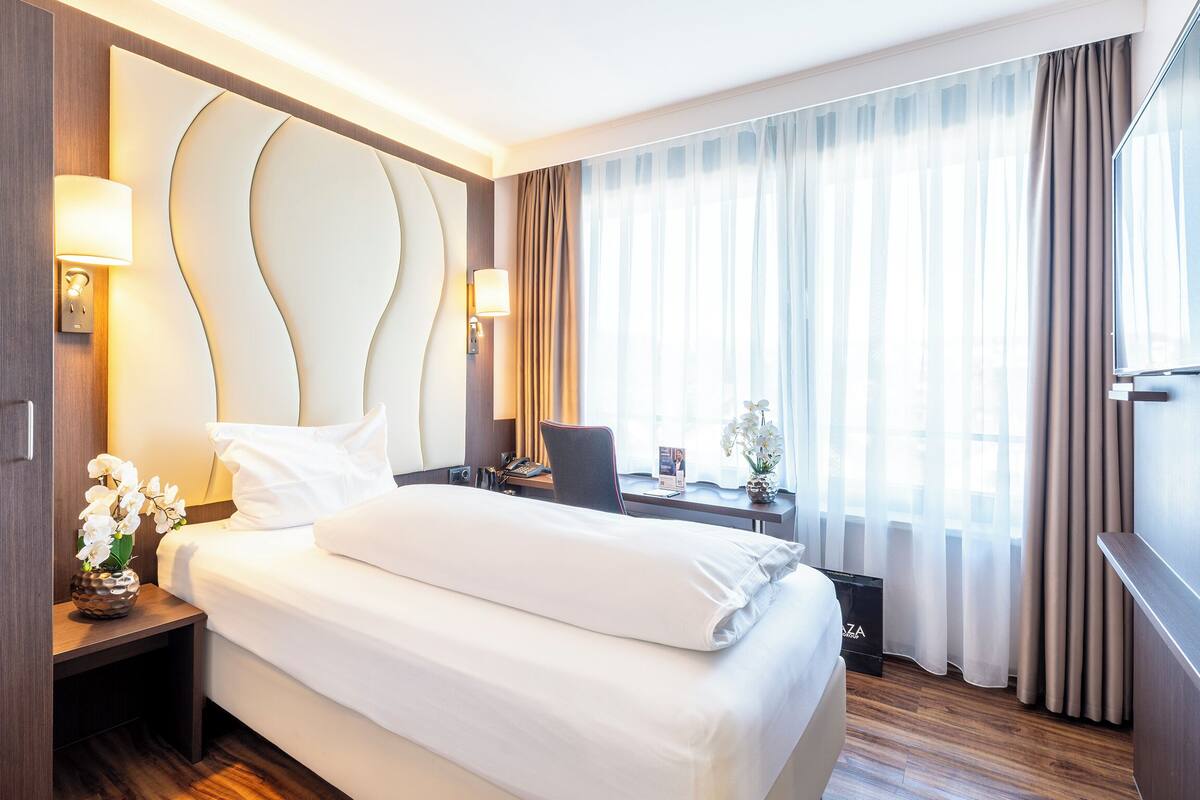 Une chambre d’hôtel avec un grand lit, un bureau, une chaise, une télévision et une fenêtre avec des rideaux.
