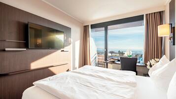 Habitación de hotel con una cama grande, un televisor de pantalla plana en la pared, un escritorio con una silla y vistas a la ciudad a través de amplias ventanas.