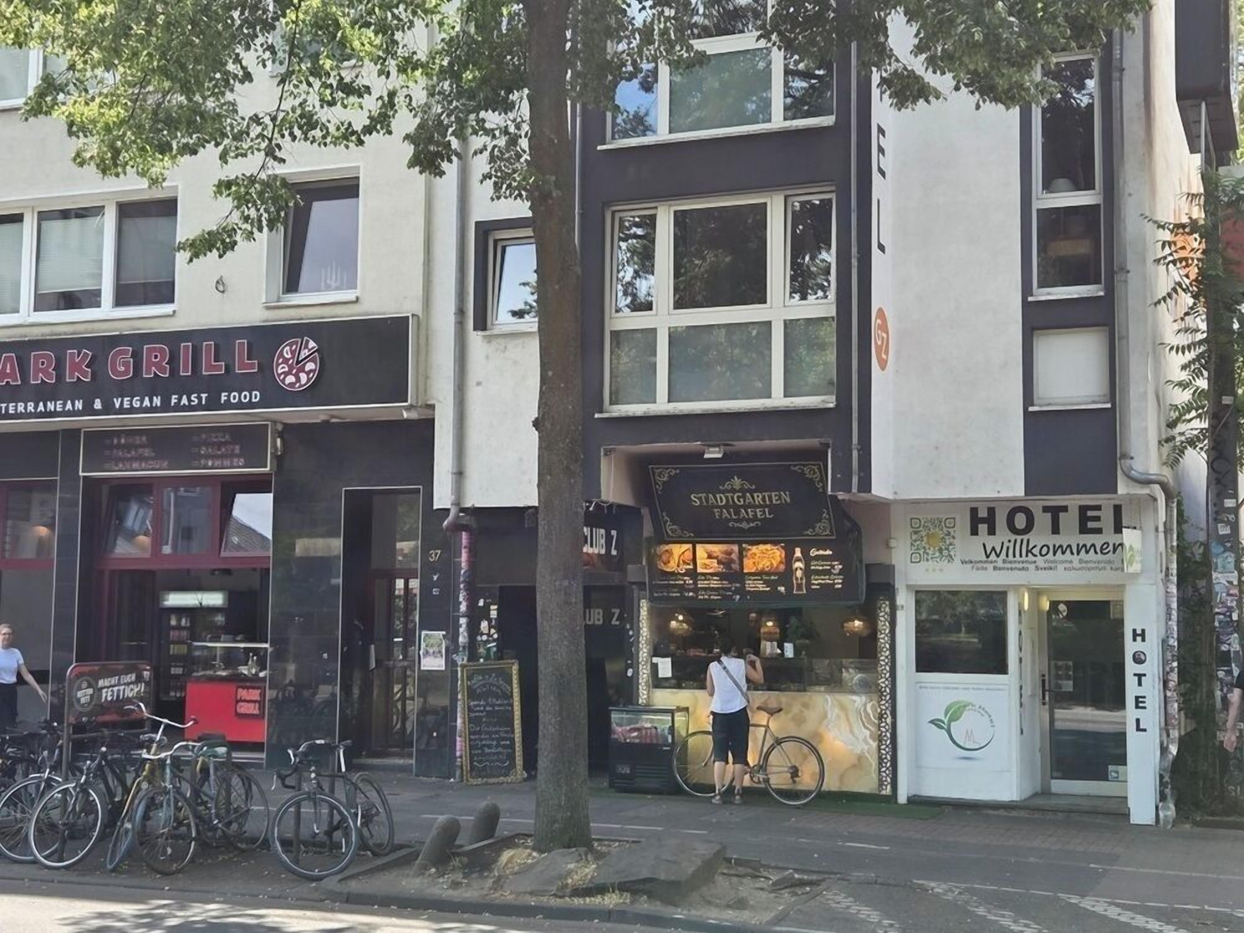 Vista da rua com um restaurante chamado 'ARKGRILL' e a placa 'HOTEL Willkommen'.