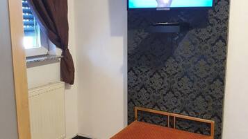 Ein Zimmer mit einem an der Wand montierten Fernseher, einer Holzbank und einer Heizung.