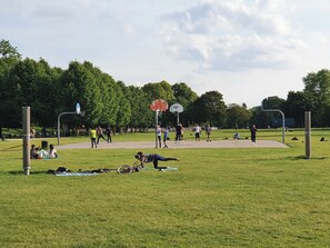 Un parc en plein air doté d’un terrain de basketball, d’arbres et où l’on peut voir des gens pratiquer diverses activités.