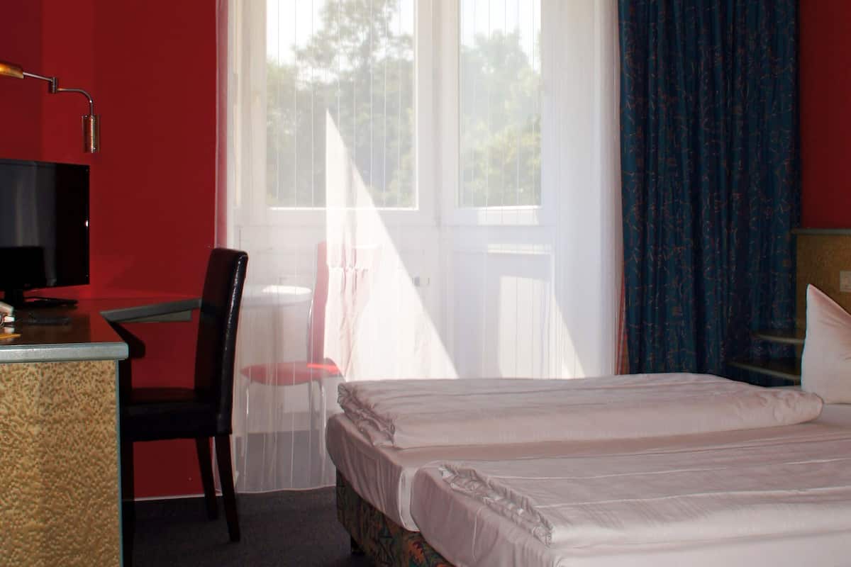 A hotel room with a bed, a desk, a chair, and a window with curtains.